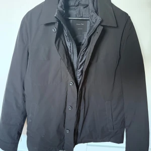 Svart jacka från Massimo dutti - Säljer en svart jacka från Massimo dutti med klassisk krage och knappar framtill. Jackan har långa ärmar, två sidofickor och en innerjacka med dragkedja. Perfekt för kyligare dagar.