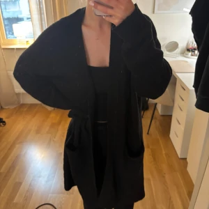 Svart lång mjuk kofta - Mysig svart cardigan jacka med oversized passform och långa ärmar. Perfekt att slänga på sig över en outfit för extra värme. Enkel och stilren design utan synliga detaljer.