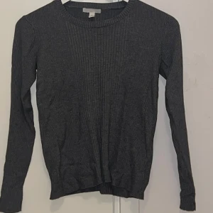 Grå ribbad tröja från H&M - En enkel och stilren grå ribbad tröja från H&M Basics. Tröjan har rund halsringning och långa ärmar, perfekt för lager-på-lager eller som den är. Mjuk och bekväm, passar till det mesta i garderoben. Finns ett litet hål i nacken som inte syns när man har på sig den. Så länge man inte öppnar hålet. Så syns den inte. Väldigt lätt att fixa också 