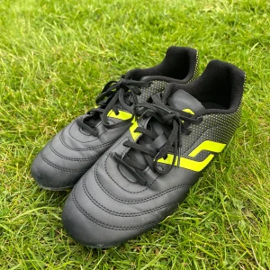 Svart/gula fotbollsskor Pro Touch - Svart/gula fotbollsskor från Pro Touch med snörning storlek 37. Använda få gånger och har inga tydliga tecken på användning mer än att sulan har börjat att forma sig lite efter foten. Dubbarna är som nya!⚽️😊