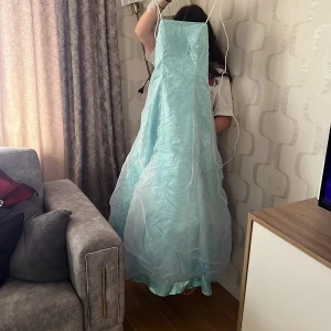 Ljusblå långklänning med paljetter - Säljer en ljusblå långklänning med glittriga paljettdetaljer och tunt tylltyg över kjolen. Klänningen har smala axelband och en elegant, svepande form som passar perfekt till bal eller fest.