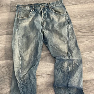 Blå Levis 501 jeans - Klassiska blå Levis 501 jeans med raka ben och knappgylf. Jeansen har en vintage tvätt med slitningar och fem fickor. Perfekta för en avslappnad stil och passar till det mesta.