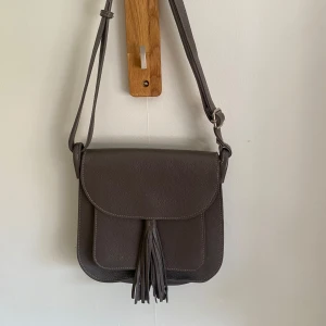 Don Donna axelväska med fransdetalj - Säljer en grå axelväska i veganskt läder från märket DonDonna med lock och dekorativ frans framtill. Väskan har justerbar axelrem, skriv till mig vid frågor! ❤️ priset kan diskuteras 