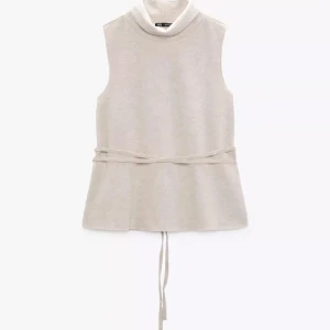 Vit ärmlös polotopp med knytband - Säljer en stilren vit ärmlös polotopp från Zara med högt krage och knytband i midjan. Perfekt att styla lager på lager eller bära som den är. Enkel och modern design.