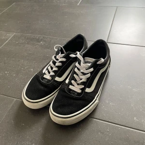 Svarta Vans Old Skool sneakers - Vans Old Skool sneakers i svart med vit sula och vit sidoremsa i storlek 38. Skorna har snörning och är tillverkade i canvas och mocka.