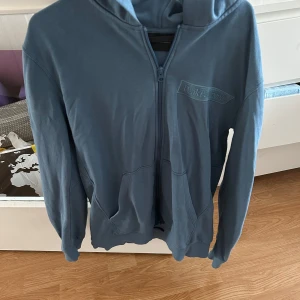 Blå hoodie från Peak Performance - Säljer en blå hoodie från Peak Performance i storlek L. Tröjan har dragkedja framtill, huva och två fickor. Perfekt för en avslappnad stil och enkel att matcha med det mesta. Btw har tappat bort snöret 