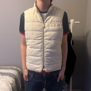 Stenströms väst - Säljer en beige quiltad väst från Stenströms med dragkedja framtill och hög krage. Västen har en bröstficka och diskret logga nedtill. Perfekt för lager-på-lager och enkel att matcha med olika outfits. Modellen är 190cm, 80kg