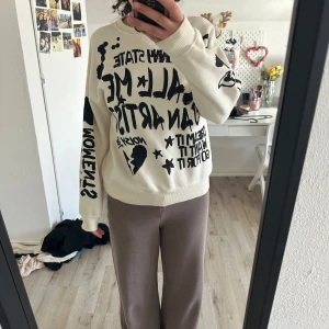 Vit sweatshirt med svart textprint från Zara - Säljer en vit sweatshirt från Zara med stora svarta tryck och text över hela tröjan. Tröjan har rund hals och långa ärmar. Perfekt för en avslappnad och cool stil.