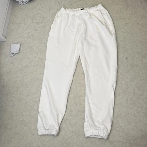 Vita mjukisbyxor från 157 - Säljer ett par vita mjukisbyxor från 157 med resår i midjan och vid bensluten. Byxorna har en avslappnad passform och är tillverkade i mjukt material, perfekta för en chill dag hemma eller till vardagslooken. Aldrig använd