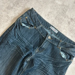 Blå bootcut jeans med broderade bakfickor - Snygga blå jeans med bootcut passform och broderade detaljer på bakfickorna. Klassisk femficksmodell med låg midja och dragkedja. Perfekta för dig som gillar en retroinspirerad stil. Använt en gång. 