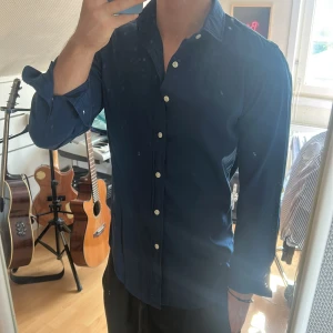 Mörkblå skjorta från Ralph Lauren - Säljer en klassisk mörkblå skjorta från Ralph Lauren med broderad logga på bröstet. Skjortan har lång ärm, vita knappar och en slim passform. Perfekt för dig som gillar stilrena plagg med snygga detaljer.