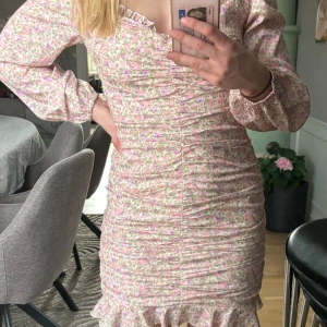 Blommig kortklänning. - Supersöt kortklänning med blommigt mönster i rosa, lila och grönt. Klänningen har långa ärmar. Super fin och enbart använd 1 gång. Inga märken.