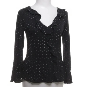 Svart prickig blus Lindex - Supersöt svart tröja från Lindex med vita prickar och volangdetaljer längs ringningen och framtill. Långärmad modell i mjukt material 💞💞 Inga tydliga tecken på användning