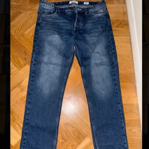 Blå jeansbyxor från Levis 501 - Klassiska blå Levis 501 jeans med rak passform och fem fickor. Byxorna har normal midja och stängs med knappar. Perfekta för en avslappnad stil.