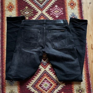 Svarta jeans från Nudie Jeans - Snyggt fadeade svart/gråa jeans från Nudie Jeans med en klassisk femficksdesign. De har en slim passform och är modellen ”tight long John”, sitter ungefär som grim tim. Jeansen är i sjukt bra skick. Nypris 1600kr. Kom med bud! Storleken är W30 L34, men sitter snarare som 32. 