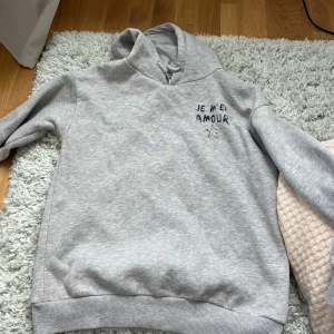 Grå hoodie med tryck 'JE M'EN AMOUR' - Säljer en ljusgrå hoodie från Gina Tricot, den är använd max 5 gånger, pris kan diskuteras 
