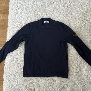 Mörkblå tröja från Stone Island - Säljer en mörkblå långärmad tröja från Stone Island med den klassiska loggan på ärmen. Tröjan har rund halsringning och är tillverkad i bomull. 