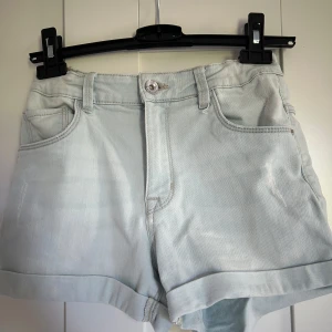Ljusblå jeansshorts med uppvik - Säljer ett par ljusblå jeansshorts från Ü i storlek 164. Shortsen har klassisk femficksdesign, knapp och dragkedja framtill samt uppvikta benslut. Perfekta för varma dagar och enkel att matcha med olika toppar.