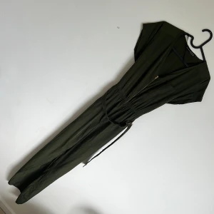 Olivgrön jumpsuit med dragkedja från Atmosphere - Snygg olivgrön jumpsuit med v-ringning och dragkedja framtill. Den har korta ärmar, markerad midja med bälte och en bröstficka. Perfekt för en avslappnad men stilren look.