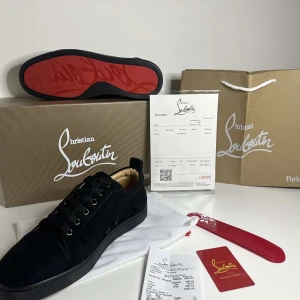 Christian Louboutin Skor - Säljer ett par svarta sneakers från Christian Louboutin med klassisk röd sula. Skorna har snörning, rund tå och är tillverkade i mocka. Perfekta för dig som vill ha en stilren och lyxig look.