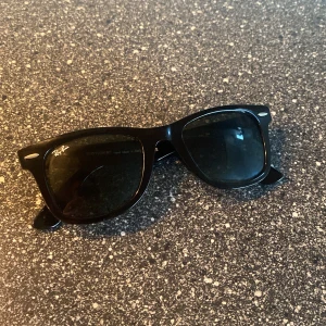Svarta solglasögon Wayfarer från Ray-Ban - Riktigt feta Wayfarer-solglasögon från Ray-Ban med bred båge och mörka glas. Ikonisk modell med Ray-Ban-logga på båda sidor. Passar perfekt för en stilren look året runt. 