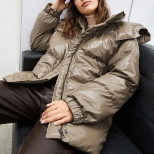 Brun pufferjacka med huva - Säljer en brun, glansig pufferjacka med stor huva och dragkedja framtill. Jackan är oversized och har långa ärmar samt breda kanaler för extra värme. Den är använd en gång men som ny. (Nypris: 830kr)