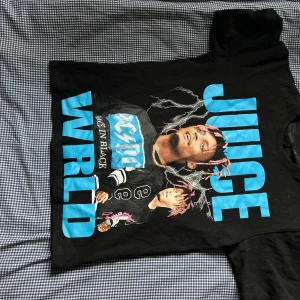 Svart Juice WRLD x VLONE t-shirt - Säljer en svart t-shirt från VLONE med stor blå Juice WRLD-tryck framtill och ett stort blått V på ryggen. T-shirten har korta ärmar och är i bomull. Perfekt för dig som gillar streetwear och vill sticka ut med en unik design.