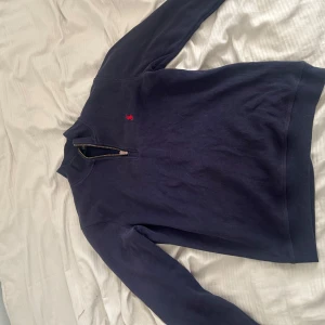 Halfzip  från Ralph Lauren - Säljer en mörkblå halfzip från Ralph Lauren med en liten röd raffe ogga på bröstet. 