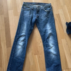 Nudie Jeans Super Slim Kim 32/32 - Säljer ett par klassiska blå jeans från Nudie Jeans, modell Super Slim Kim. Jeansen har en slim passform, fem fickor och snygga slitningar framtill. Tillverkade i bomull med orangea sömmar och Nudie-logga på bakfickorna.