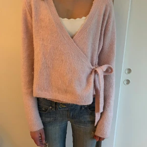 Ljusrosa omlottkofta med knytband från Gina 💕 - Säljer en supermjuk och fluffig ljusrosa omlottkofta med knytband i sidan. Koftan har lång ärm och v-ringad halsringning, perfekt att slänga på sig över ett linne eller t-shirt. Snygg och enkel att styla till jeans eller kjol. Den är lite noppig 💕✨