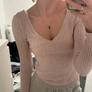 Ljusrosa ribbad topp från Bik Bok - Säljer en ljusrosa ribbad långärmad topp från Bik Bok med v-ringning både fram och bak. Toppen är tight och har en mjuk, stretchig känsla. Perfekt att styla med jeans eller kjol för en trendig look.