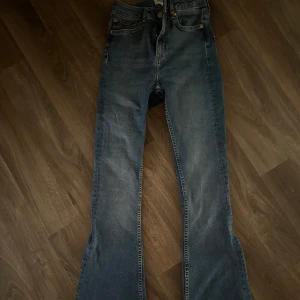 Blå bootcut jeans - Säljer ett par klassiska blå bootcut jeans med hög midja. Jeansen har fickor, dragkedja och knapp framtill samt utsvängda ben. Perfekta för dig som gillar en retroinspirerad look. De är väldigt små i storlek och passar xxs. Använda två gånger 🤍🌸