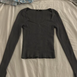Grå ribbad topp från Gina Tricot - Säljer en grå, ribbad långärmad topp från Gina Tricot. Modellen är figurnära med en snygg, något djupare urringning och stretchigt material. Perfekt att styla med jeans eller kjol för en trendig look.