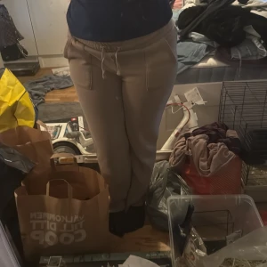 Beige mjukisbyxor med dragsko - Säljer ett par beige mjukisbyxor i storlek L med resår och dragsko i midjan. Byxorna har två stora fickor framtill och är perfekta för en avslappnad stil. Mjukt material som känns skönt mot huden.