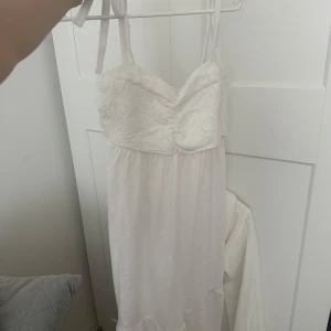 Klänningar  - Säljer en långärmad omlottklänning med färgstarkt mönster i vinrött, rosa, blått och vitt. Klänningen har djup v-ringning, knyt i midjan och en slits framtill. Perfekt för dig som vill sticka ut med en unik look.