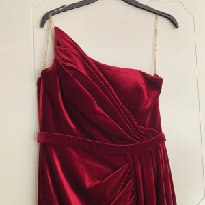 Vinröd sammetsklänning med snörning - Säljer en vinröd långklänning i sammet med smala axelband och draperad framsida. Klänningen har markerad midja, slits och snygg snörning i ryggen. Perfekt för bal eller fest. Snygg och elegant look!