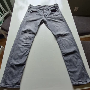 Grå jeansbyxor från Replay - Säljer ett par grå jeansbyxor från Replay med klassisk femficksdesign och raka ben. Byxorna har svarta detaljer vid linningen och en diskret Replay-logga vid bakfickan. Perfekta för en stilren vardagslook. Riktigt stilrena! 