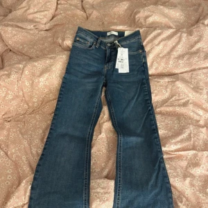 Blå bootcut jeans från gina tricot  - Säljer ett par klassiska blå bootcut jeans från Gina tricot med låg midja. Jeansen har fem fickor, dragkedja och knapp framtill. Perfekta för dig som gillar en tidlös och avslappnad stil.💞💞