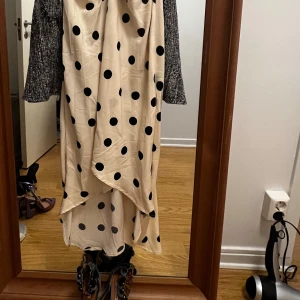 Prickig omlottklänning med puffärm - Snygg beige klänning med svarta prickar och v-ringning. Klänningen har puffärmar, omlottdesign och rynkade detaljer framtill. Perfekt för dig som gillar trendiga och lekfulla plagg.