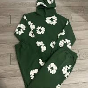 Gröna mjukisbyxor med vita blommor från Denim Tears - Säljer ett par gröna mjukisbyxor från Denim Tears med vita blommor tryckta över hela byxorna. Byxorna har resår i midjan och en avslappnad passform, perfekta för en chill och trendig look.