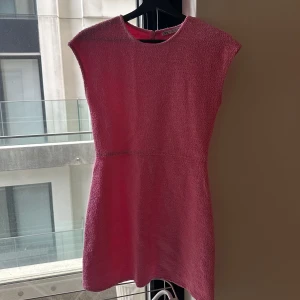 Rosa kortklänning med struktur - Säljer en söt rosa kortklänning med rund hals och ärmlös design. Klänningen har en lätt strukturerad yta och markerad midja för en feminin siluett. Perfekt för sommarens alla tillfällen!