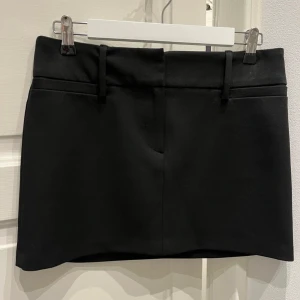 Svart minikjol - Enkel och stilren svart minikjol med bälteshällor i midjan. Kjolen har en rak passform och är perfekt för att skapa en clean look. Passar till många olika stilar och är lätt att matcha med olika toppar.