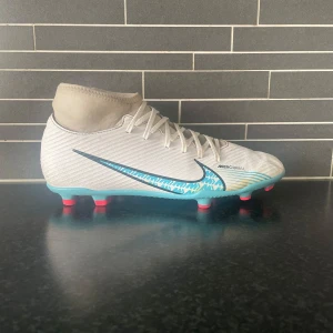 Nike Mercurial fotbollsskor i vitt och blått - Säljer ett par Nike Mercurial fotbollsskor i vitt med blå detaljer.Perfekta för dig som vill sticka ut på planen! Väldigt fint skick i storlek 41. Hör av dig vid minsta fundering✅🙌