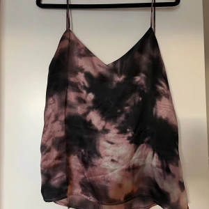 Linnetopp i batikmönster från NLY Trend - Säljer en snygg linnetopp från NLY Trend i lila och svart batikmönster. Toppen har tunna axelband och v-ringning framtill samt knytning i ryggen. Perfekt för sommaren och enkel att styla till olika looks.