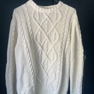 Vit stickad tröja från Morris Gents - Säljer en vit stickad tröja från Morris Gents med snyggt kabelstickat mönster framtill och på ärmarna. Tröjan har rund halsringning och ribbade muddar. Perfekt för lager-på-lager under kyliga dagar.