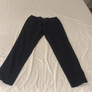 Svarta byxor från River Island - Säljer ett par svarta byxor från River Island med elastisk midja. Byxorna har en rak passform och är tillverkade i ett lätt, bekvämt material. Perfekta för en stilren och enkel look.