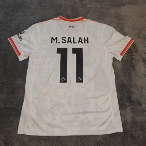 Liverpool FC | Salah | 24/25 | Ny - Liverpools tredjetröja för säsongen 2024-2025. Salah, nr 11 på ryggen. Stadium/fan edition. Ny & oanvänd. Storlek large. Tröjan är en replika i utmärkt kvalitet.  Skickas 1-3 dagar efter mottagen betalning. Har du frågor/funderingar är det bara att höra av dig! :)