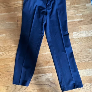 Mörkblå kostymbyxor - Snygga mörkblå kostymbyxor från Turo med klassisk rak passform och pressveck. Byxorna har midjehällor och stängs med knapp och dragkedja. Perfekta för en dressad look och passar till kavaj som säljs separat! Nypris 2500kr säljs för 500kr då han som ägde dessa avled hastigt! Knappt använda max två gånger. Köparen står för frakt