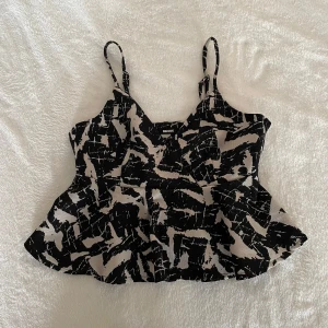 Svart och beige mönstrad linnetopp från Bik Bok - Säljer en snygg linnetopp från Bik Bok i svart och beige med abstrakt mönster. Toppen har smala axelband och en lätt utsvängd form nedtill - Jag har 20% bundle rabatt om du köper 2 plagg 🦋