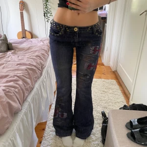 Lågmidjade bootcut jeans med patchwork & nitar - Intressekoll på dessa skitsnygga mörkblå/lila lågmidjade bootcutjeansen med slitningar och patchwork av pärlor och färg i rött och blått. Jeansen har nitar vid fickorna och runt hela midjan. Endast använda fåtal gånger & går ej att köpa nån annan stans💥❣️PRIS GÅR ATT DISKUTERA